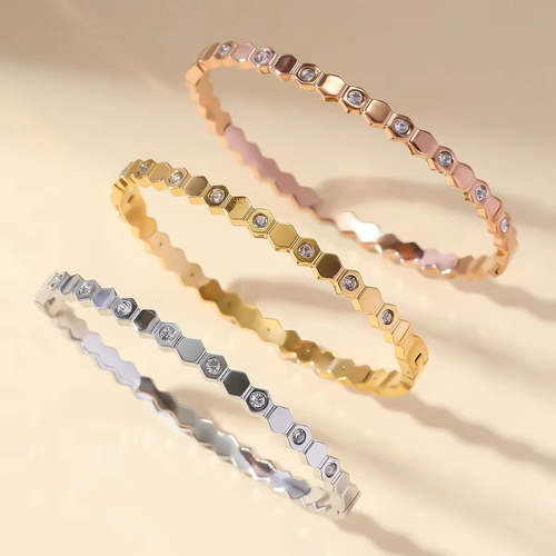 Three gold, rose gold, and silver bracelets with diamond-like stones on a beige background