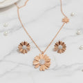 Rose gold flower-shaped necklace and earrings on a marble surface with pearls.