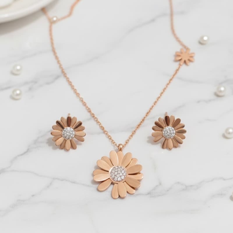Rose gold flower-shaped necklace and earrings on a marble surface with pearls.