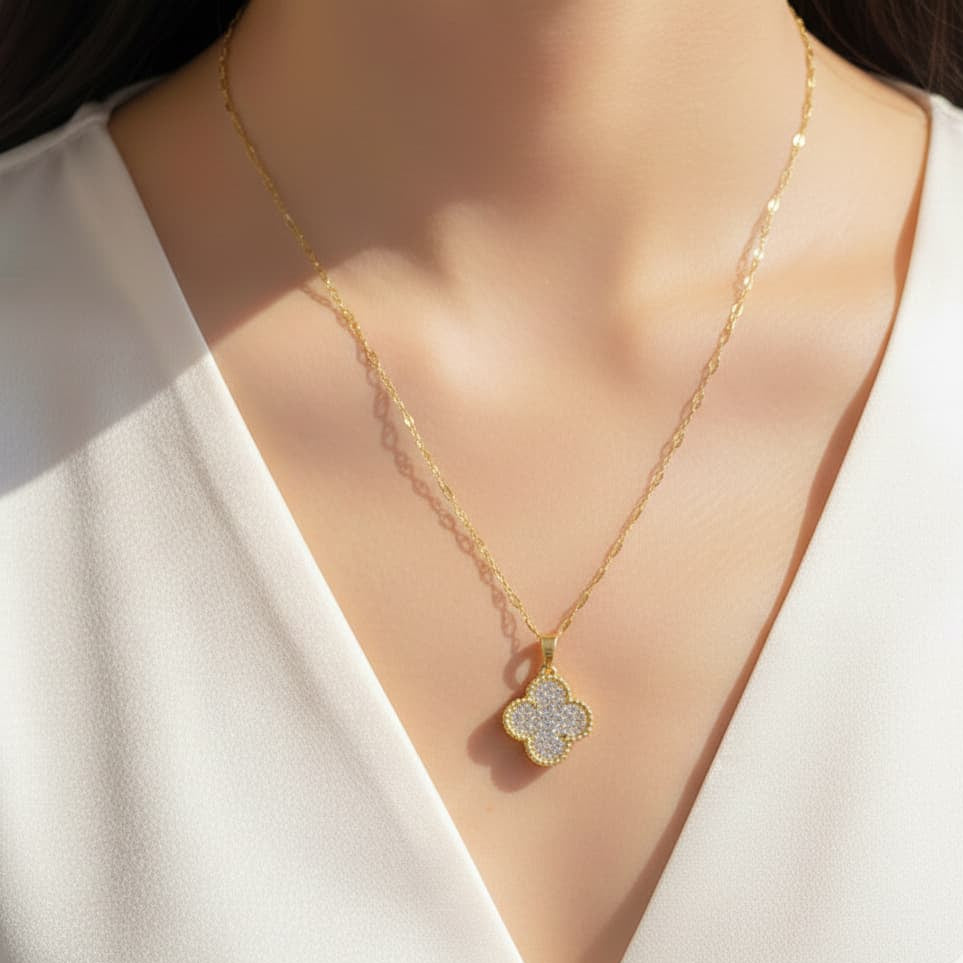 Gold necklace with a clover-shaped pendant worn by a person in a white top.