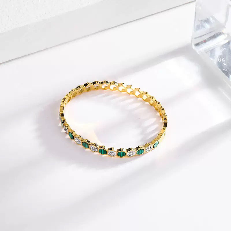 Gold bracelet with green and clear stones on a white surface