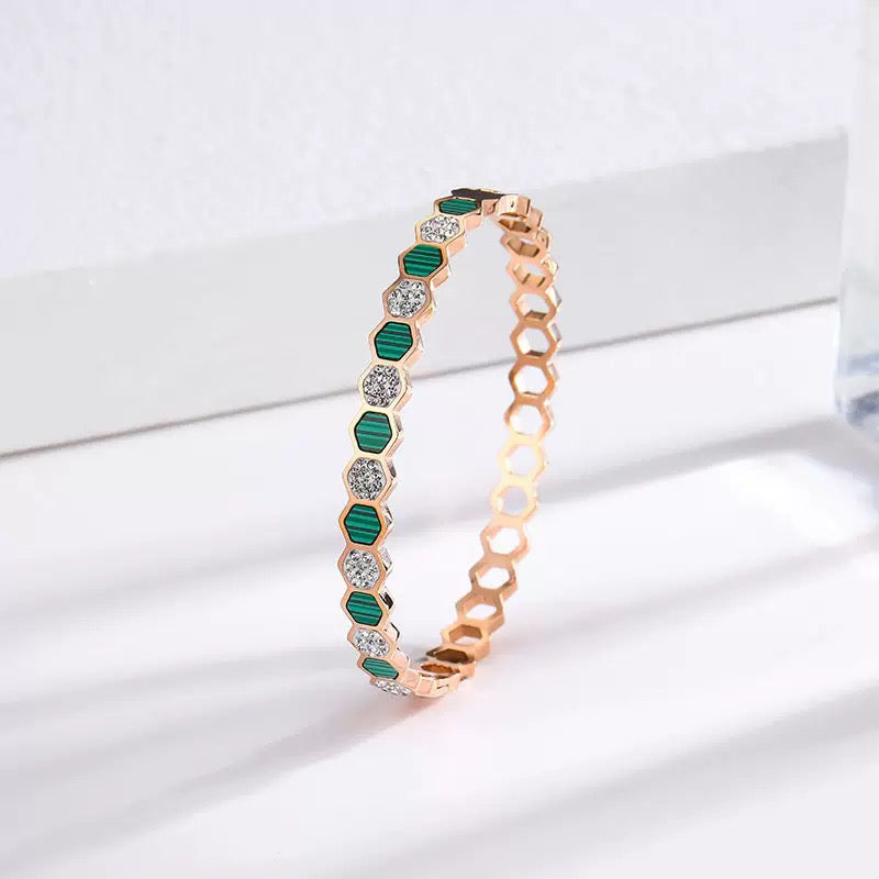 Rose gold bracelet with green gemstones on a white background