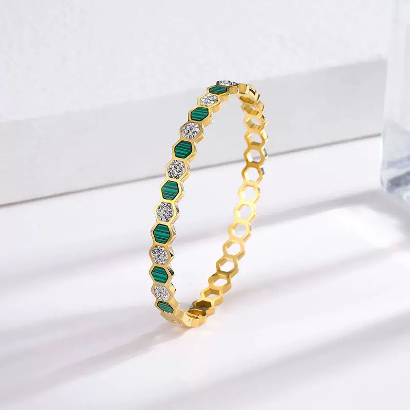 Gold bracelet with green and clear gemstones on a white background