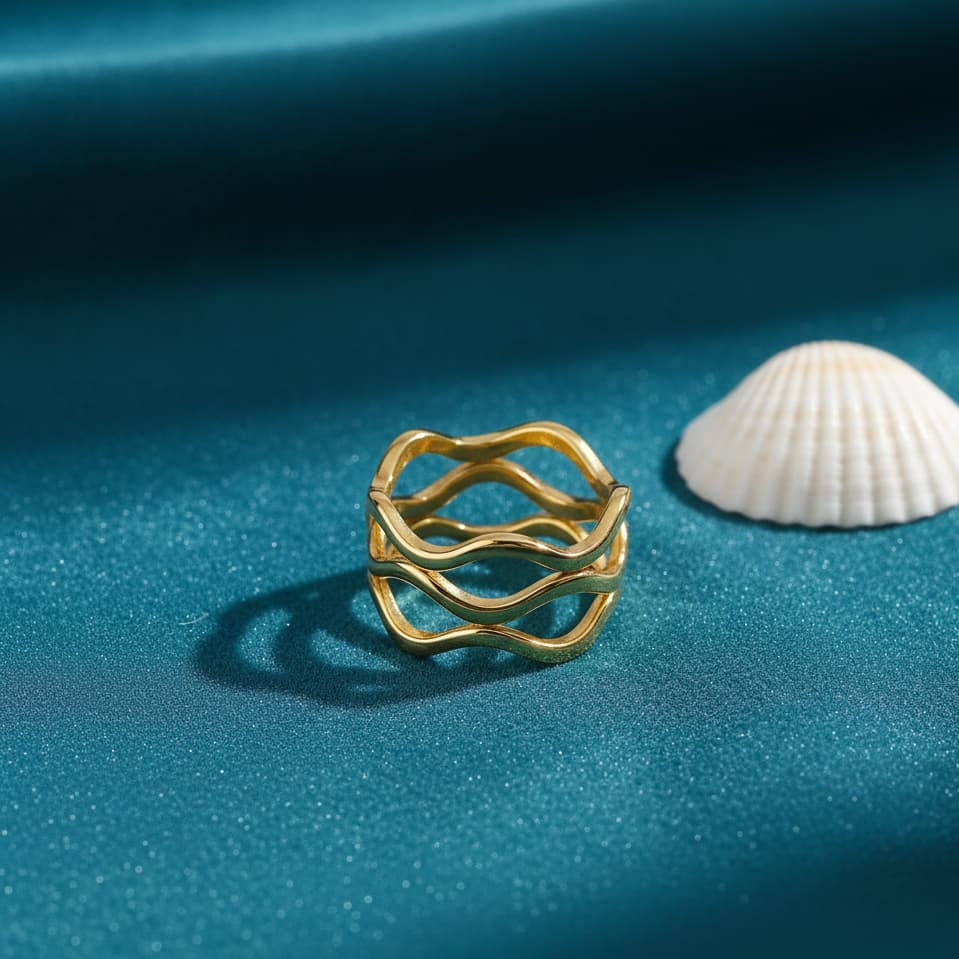 Gold ring with wavy design on a blue fabric background with a shell.