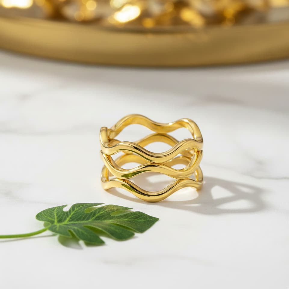 Gold ring with wavy design on a white surface with a green leaf