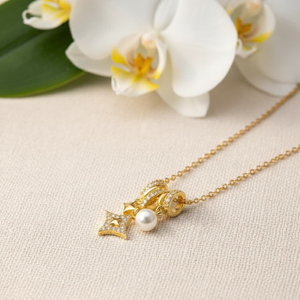 Gold necklace with a pearl pendant on a beige surface with white flowers in the background