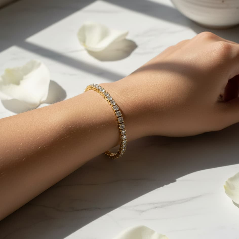 Hand wearing a gold bracelet on a light surface with white petals