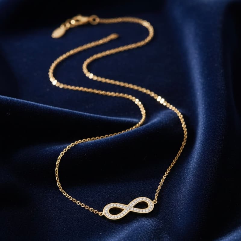 Gold infinity necklace on a dark blue fabric background