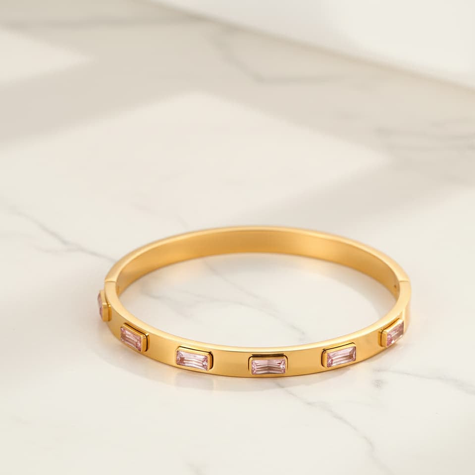 Gold bracelet with pink gemstones on a light beige background