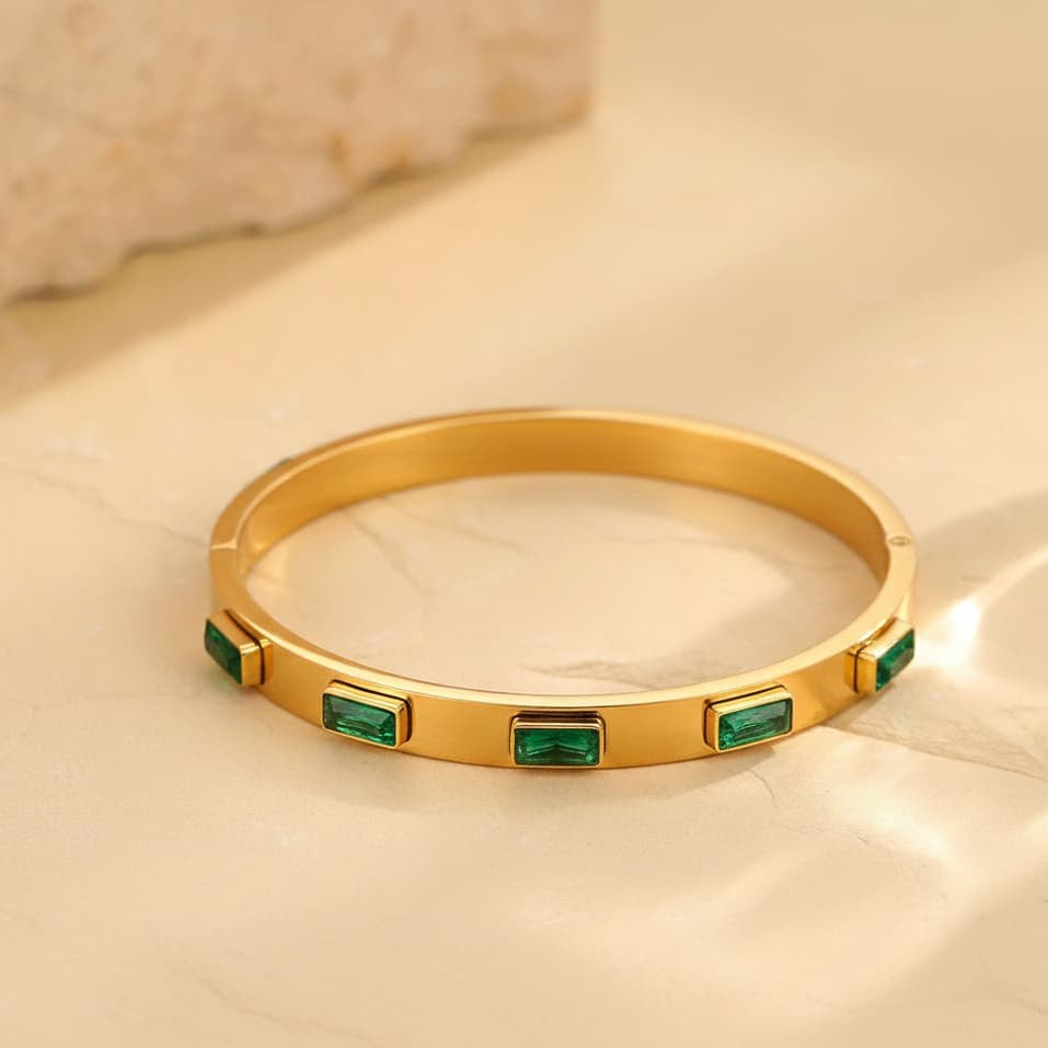 Gold bracelet with emerald stones on a beige surface