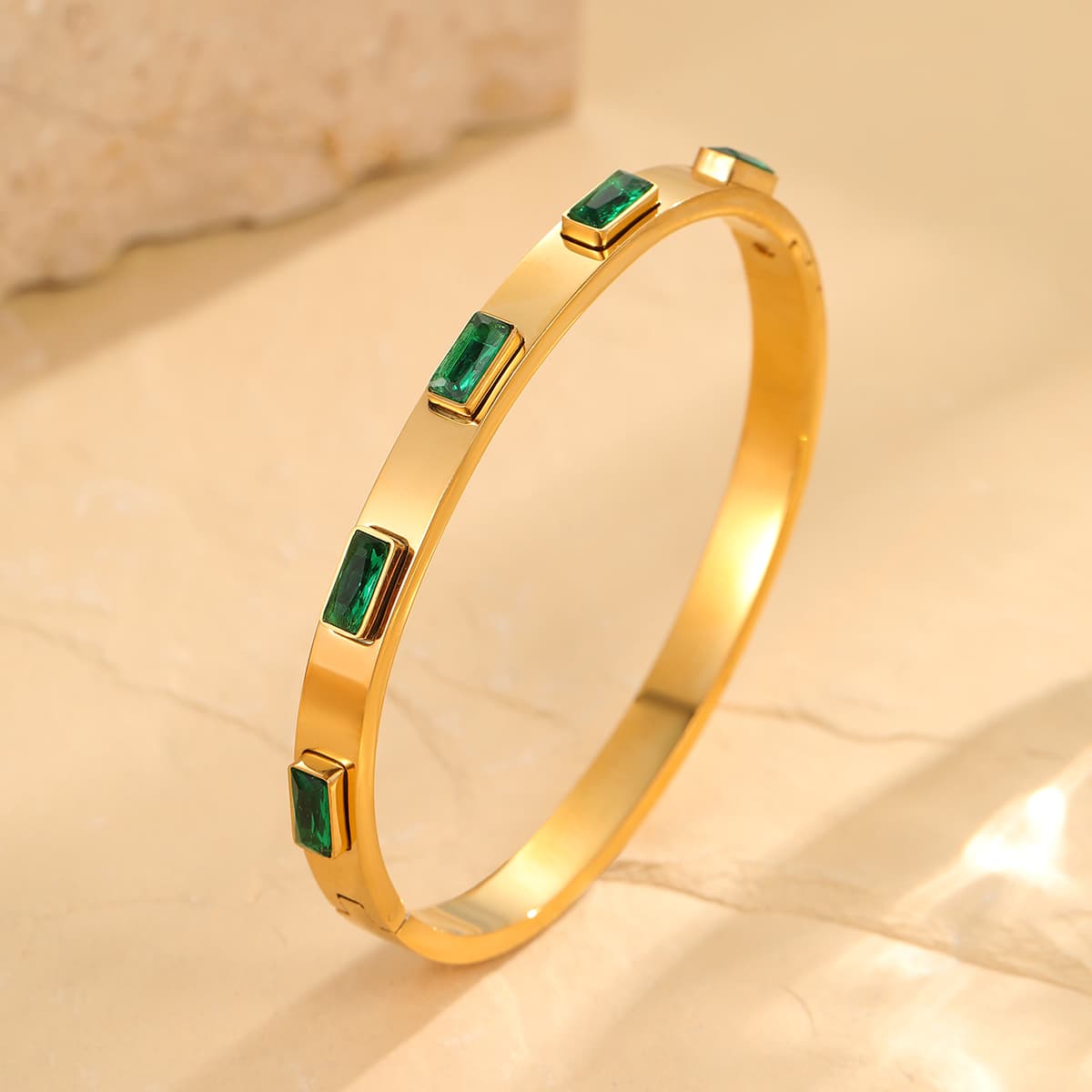 Gold bracelet with green gemstones on a beige surface