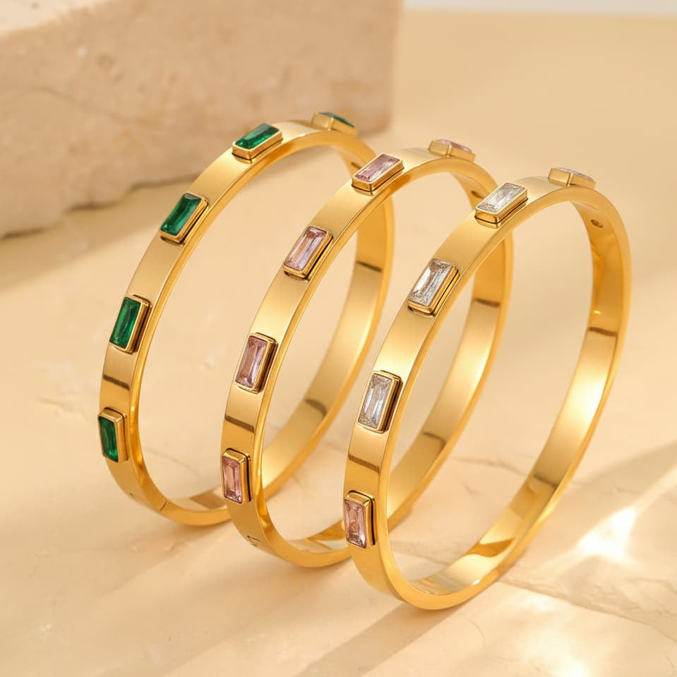 Gold bangles with gemstone accents on a beige background