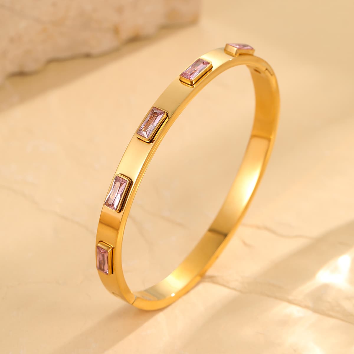 Gold bracelet with pink gemstones on a beige background