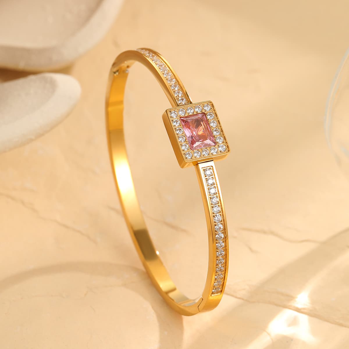 Gold bracelet with a pink gemstone on a beige background